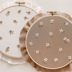 two embroidered hoops with flowers on them sitting next to each other, one in white and the other in beige