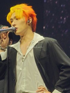 a man with orange hair is singing into a microphone