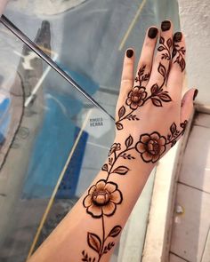 a woman's hand with henna tattoos and flowers on her left wrist, next to a glass door