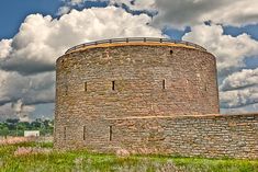 an old brick tower sitting on top of a lush green field under a cloudy blue sky