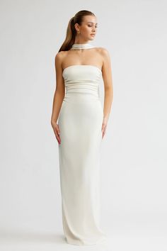 a woman wearing a white dress with a halter neckline and long skirt, standing in front of a white background