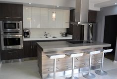 a modern kitchen with stainless steel appliances and white counter tops, along with bar stools