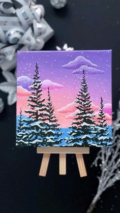 an easel with a painting on it next to some snow and christmas decorations in the background