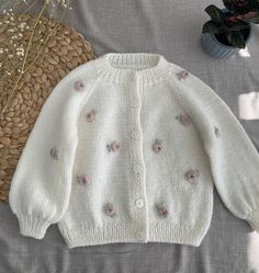 a white sweater with pink flowers on it next to a straw hat and plant in a basket