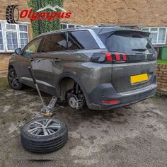 a grey car parked in front of a brick building with the back tire removed from it