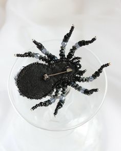 a spider made out of black beads in a wine glass with a needle stuck into it