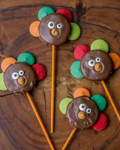 three chocolate covered turkey lollipops sitting on top of a wooden table next to two orange and green sticks