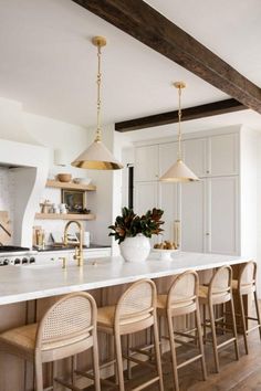 a large kitchen with white counter tops and wooden chairs in front of an island that has gold pendant lights hanging from the ceiling