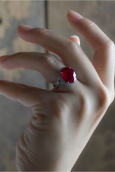 a woman's hand holding a ring with a large red stone in the middle