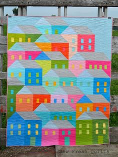 a colorful quilt hanging on a wooden fence with houses painted on the front and sides