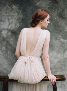 a woman in a white dress sitting on a wooden bench with her back to the camera