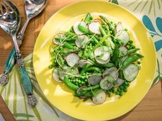 a yellow plate topped with peas and radishes next to two silver spoons