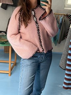 a woman taking a selfie while wearing a pink sweater and jeans with her hands in her pockets