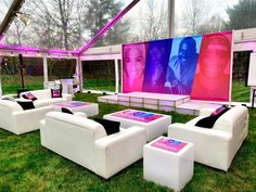 a group of white couches sitting on top of a lush green field next to a giant screen