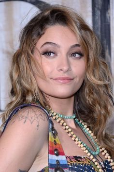 a woman with long hair wearing a multicolored dress and pearls on her neck