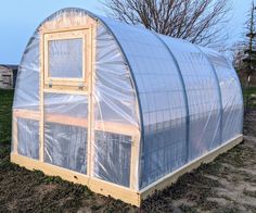 a small greenhouse with plastic covering on the roof and side walls, sitting in a field