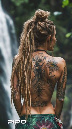 a woman with long dreadlocks standing in front of a waterfall and looking at the water