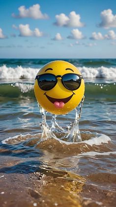 a yellow ball with sunglasses on it is in the water at the beach and has its tongue out