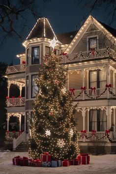 a large christmas tree in front of a house with lights and presents on the porch