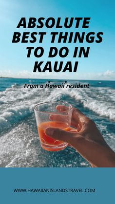 someone holding up a drink in front of the ocean with text that reads absolute best things to do in kauai from a hawaii resident