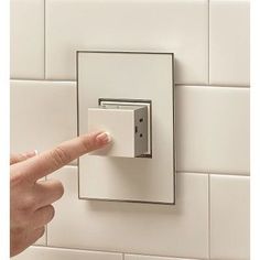 a person pressing the button on a wall mounted light switch in a white tiled bathroom