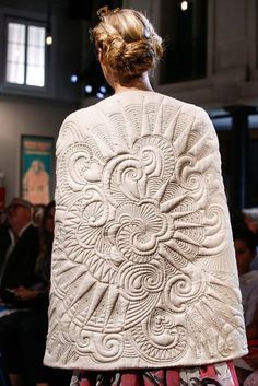 the back of a woman's white jacket with intricate designs on it at a fashion show