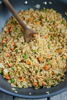 rice with peas and carrots being cooked in a skillet on a wooden table