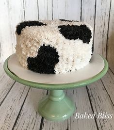 a cake with black and white frosting is on a green plate in front of a wooden wall