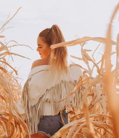 a woman standing in the middle of a corn field wearing a fringed shawl