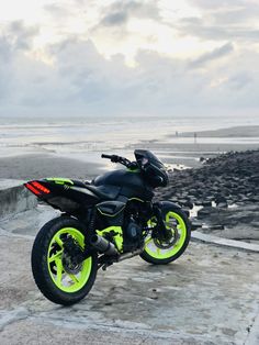 a black and yellow motorcycle parked on top of a cement slab next to the ocean