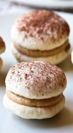 three cookies with powdered sugar on them sitting on a white plate next to other pastries