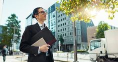 a man in a suit and tie holding a binder while standing on the street