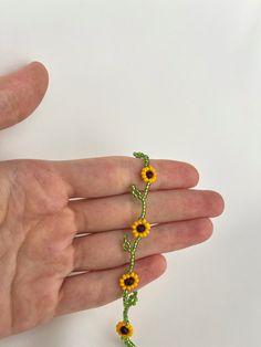 a hand holding a beaded bracelet with yellow flowers on it and green leaves in the middle