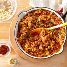 a large bowl filled with food next to bowls of spices and seasonings on a wooden table