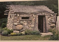 an old stone building with a small door and window in the middle of some grass