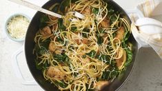 a skillet filled with pasta and chicken on top of a white countertop next to a bowl of grated parmesan cheese