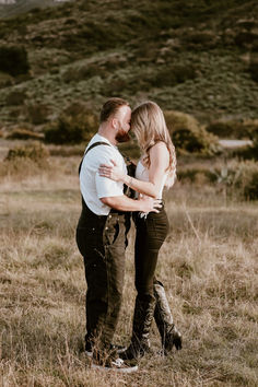 a man and woman standing in a field with their arms around each other as they kiss