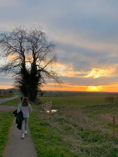 a woman walking down a path towards the sunset