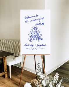 a welcome sign is on an easel in front of a couch and table with flowers