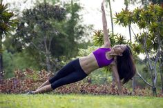 a woman in a purple top is doing a yoga pose on the grass with her hands behind her head