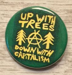 up with trees down with capitalism pinback button on white fabric, showing yellow and green lettering