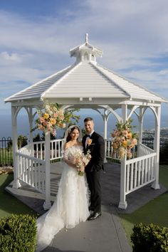 a bride and groom standing under a white gazebo