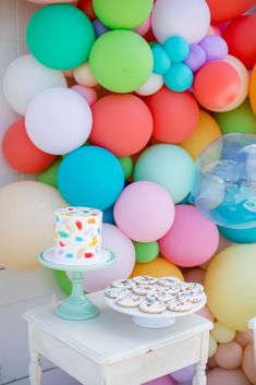 there is a cake and cupcakes on the table in front of balloon wall