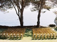 rows of wooden chairs set up in front of trees by the water's edge