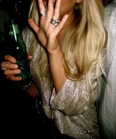 a blonde woman holding a green bottle in her right hand and making a weird face