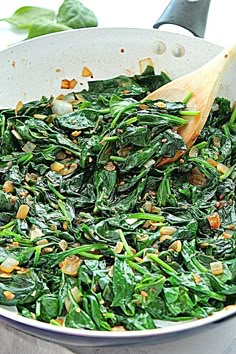 spinach and pine nuts are being cooked in a skillet with a wooden spoon