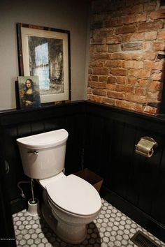 a white toilet sitting in a bathroom next to a brick wall and tiled flooring