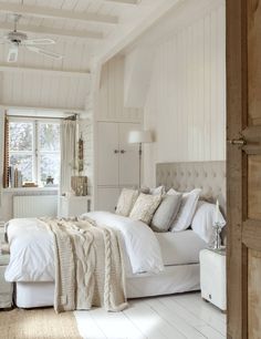 a white bed sitting in a bedroom next to a wooden door with windows on both sides