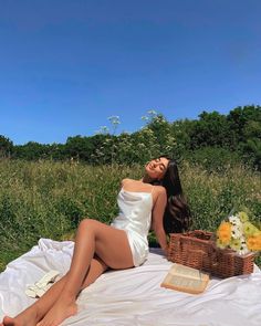 a woman sitting on top of a white blanket next to a basket filled with flowers