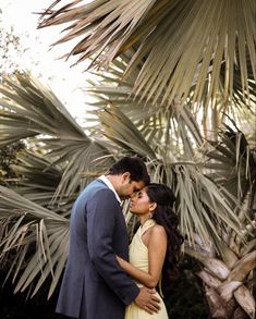 a man and woman standing next to each other in front of some palm tree leaves